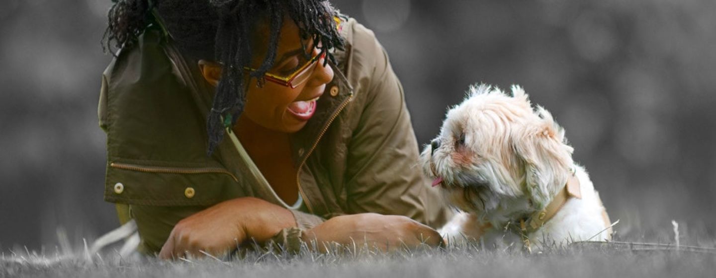 une maîtresse et son chien sont couchés dans l'herbe, ils se regardent dans les yeux.